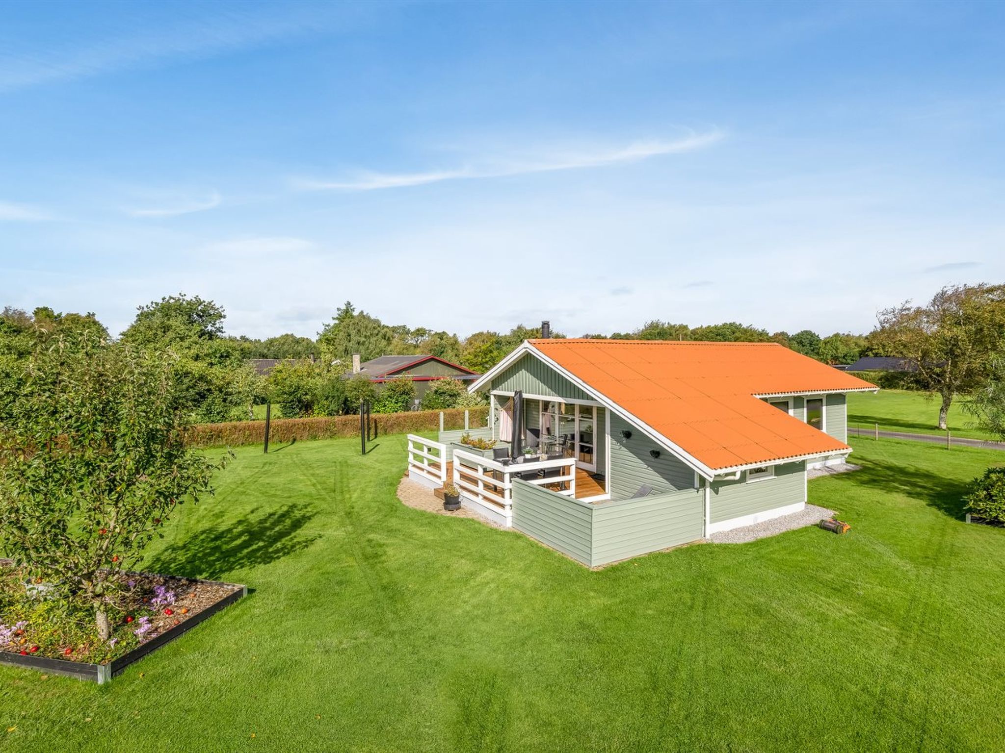A single-story house with a red roof, a deck, and a well-maintained lawn.