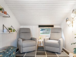 Une pièce avec deux fauteuils gris, une petite table sur laquelle se trouve un vase, une fenêtre avec des stores et un radiateur.