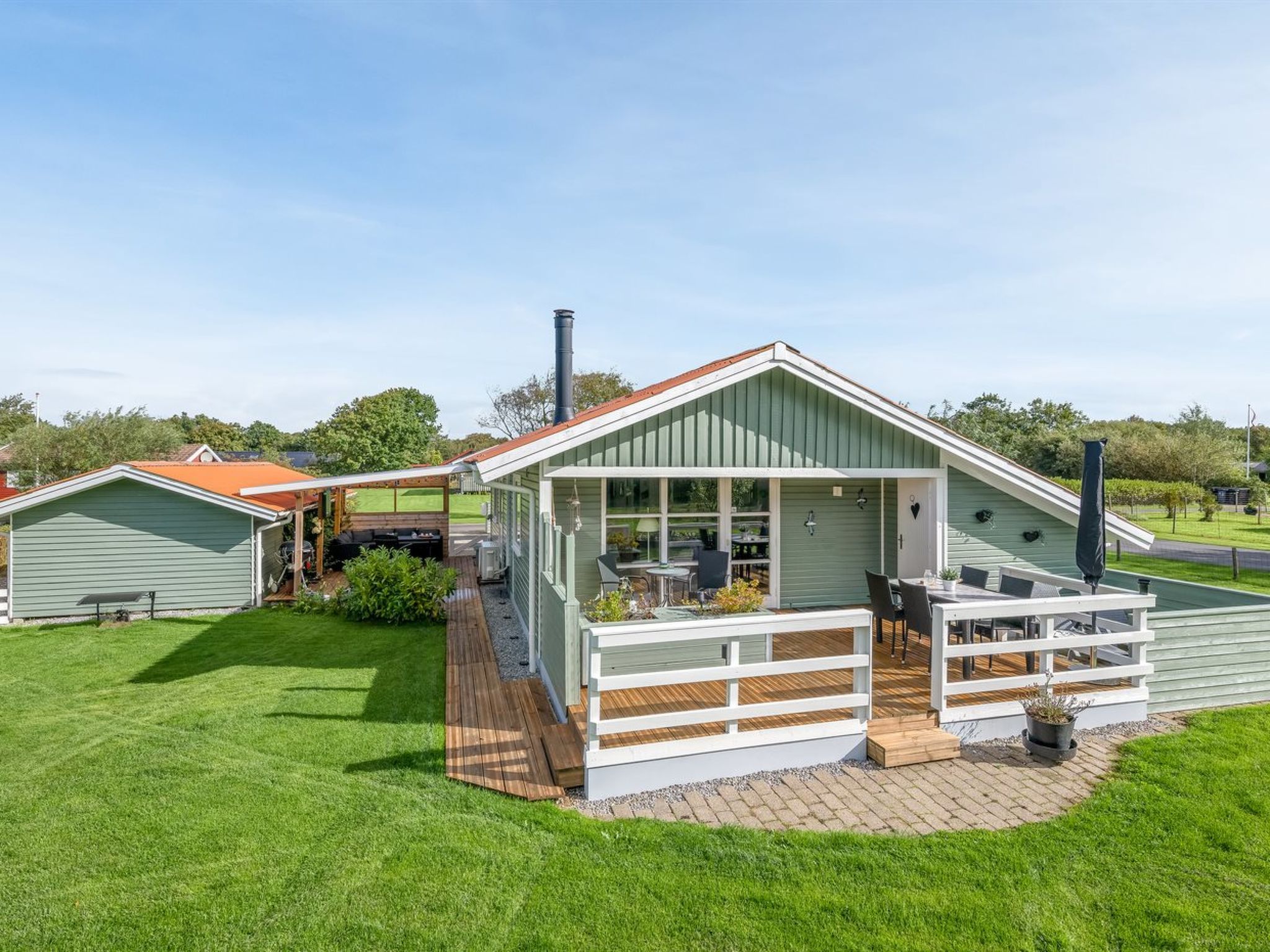 Ett modernt hus med en uteplats, ett takförsett utomhusområde och en grön gräsmatta.