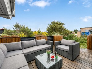 A patio with a grey sofa set, wicker chairs, and a glass-top coffee table.
