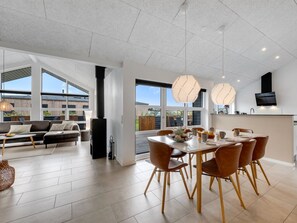 A spacious living area with a dining table, sofa, and large windows.