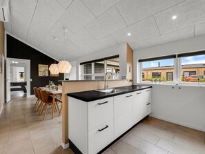 A modern kitchen with a central island, white cabinetry, and a dining area with wooden chairs.