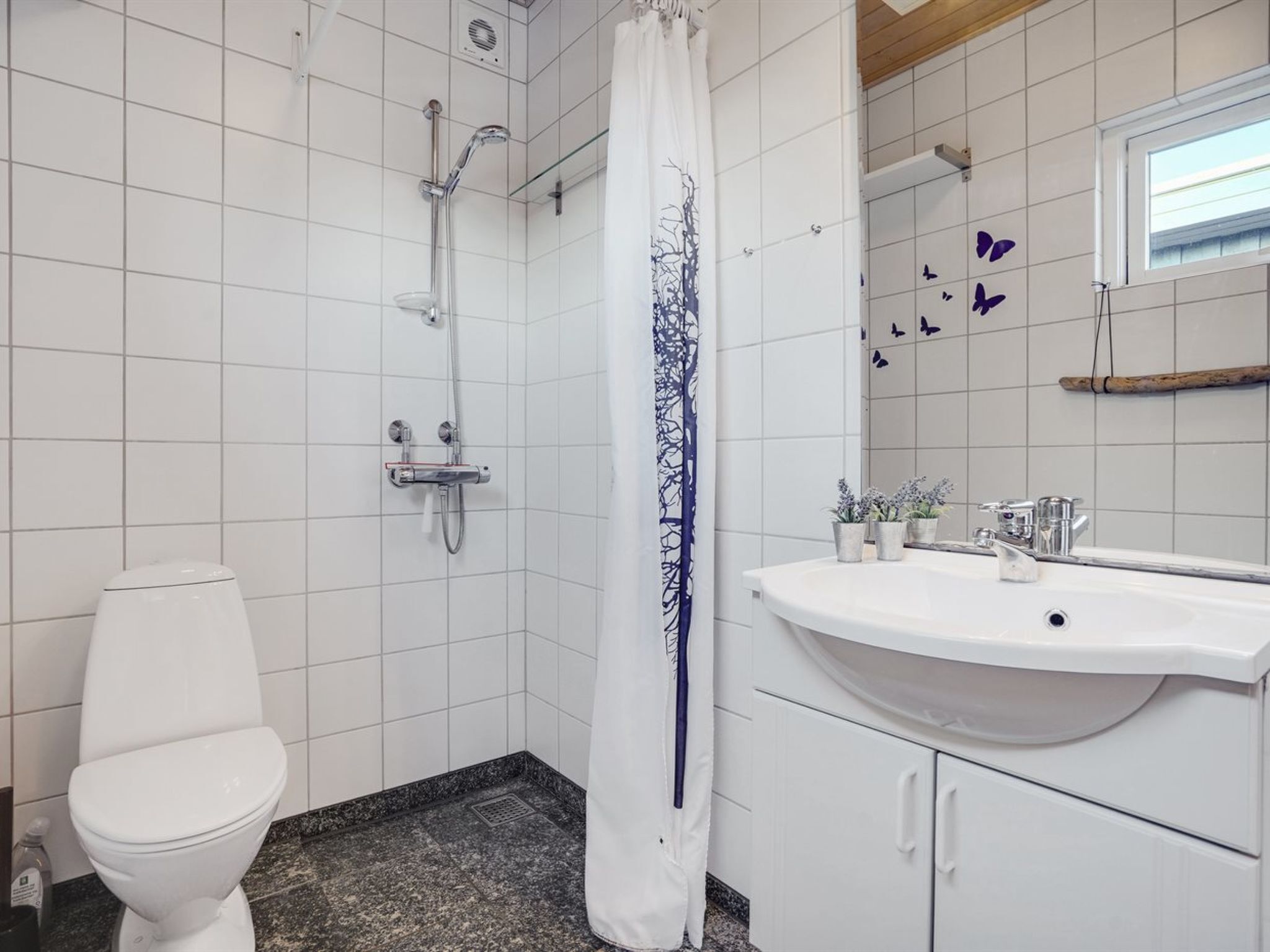 A bathroom with a white toilet, a shower with a glass door, a sink with a mirror, and decorative butterfly tiles.