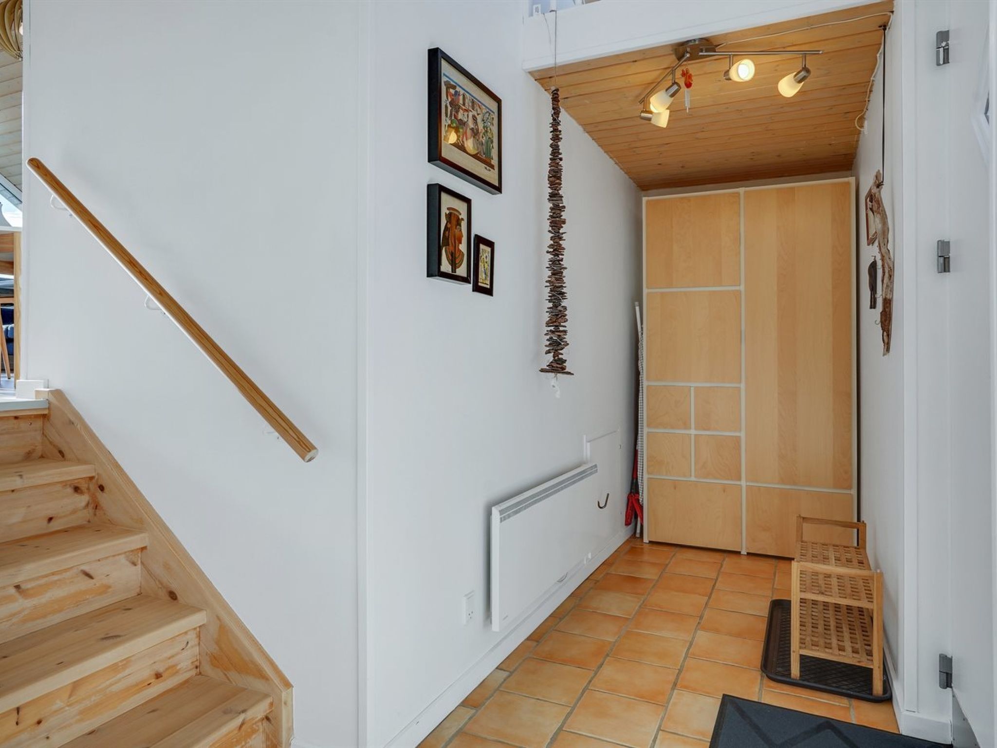 A wooden staircase leading to a room with a white wall, a radiator, and a door with a wooden panel.