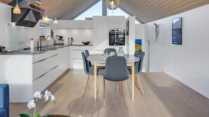 Una cocina moderna con armarios blancos, un comedor con mesa y sillas redondas, y un techo de madera.