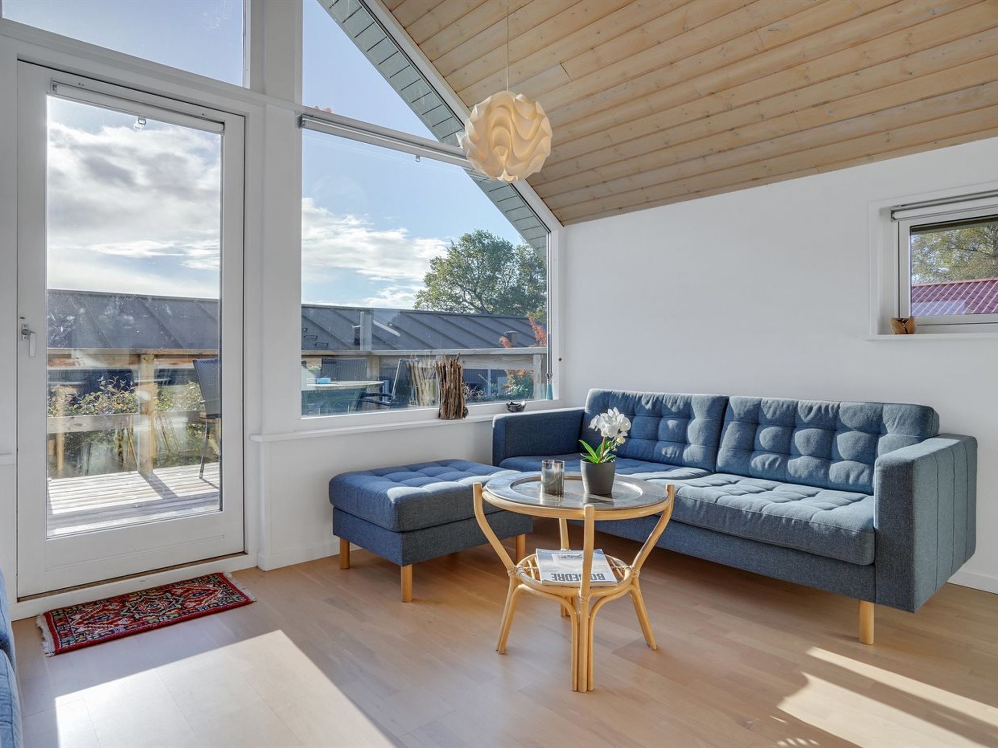 Un salon moderne avec un canapé bleu, une table ronde en verre et un plafond en bois.