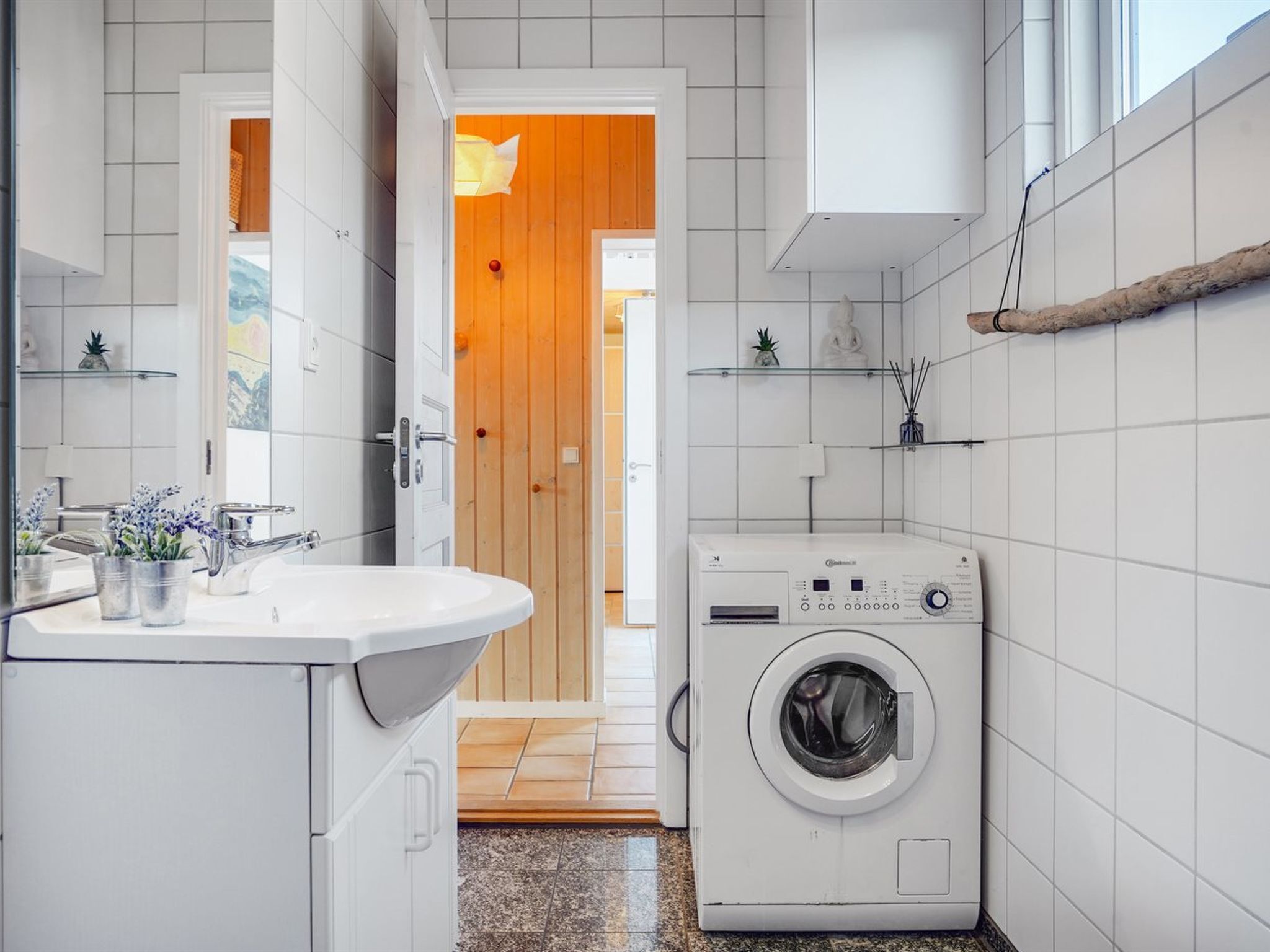 Une salle de bain moderne avec un lavabo blanc, un lave-linge et une porte en bois donnant sur une autre pièce.