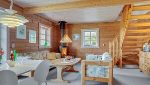 Een gezellig interieur van een chalet met houten details, een eettafel, stoelen, een bank, een open haard en een trap.