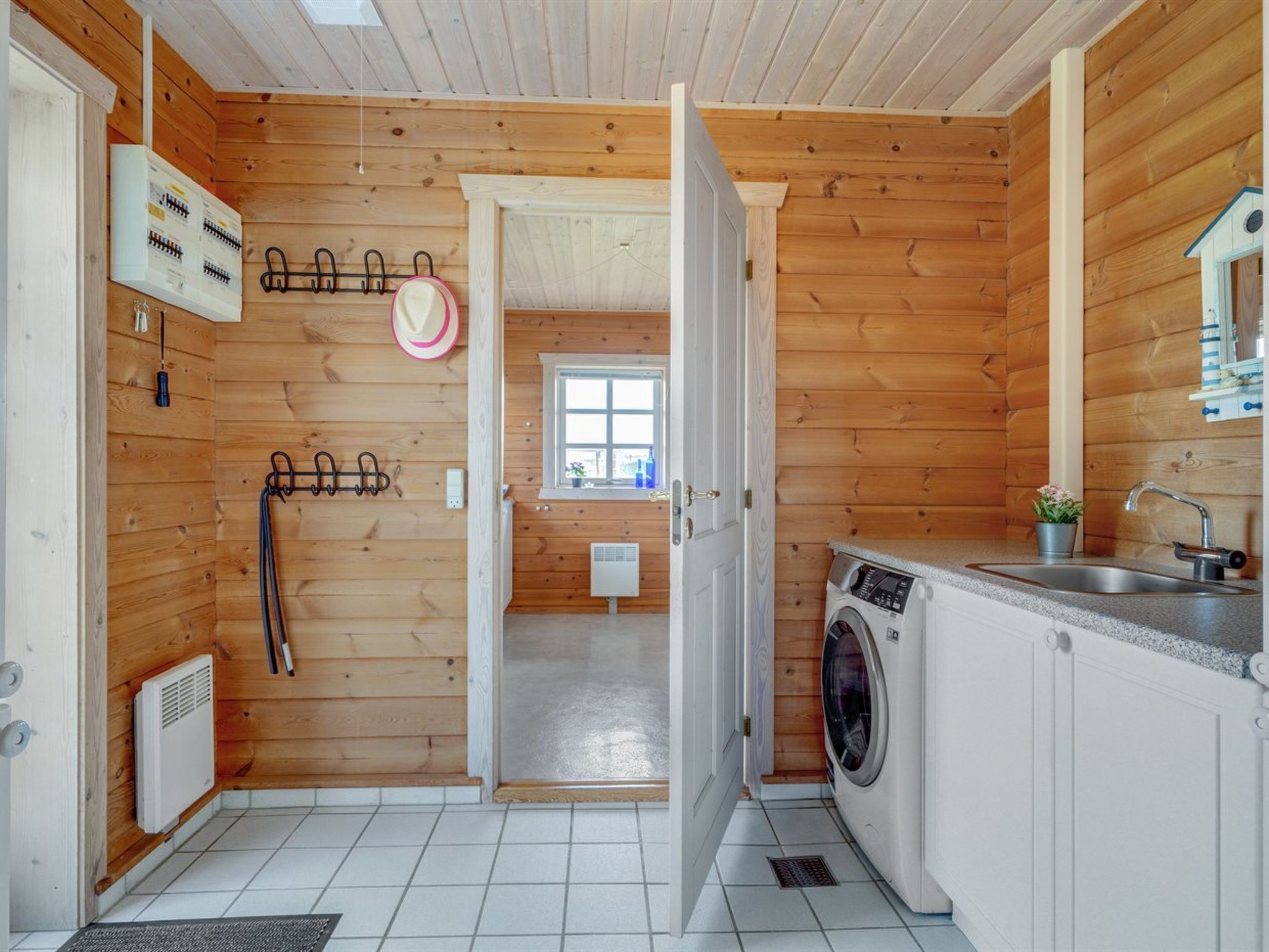Pequeña lavandería con paneles de madera, lavadora, una ventana y un radiador.