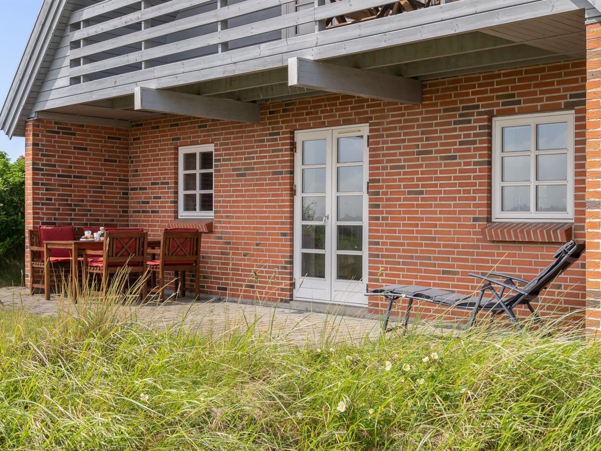 A brick house with a covered patio, a dining table with chairs, and a lounge chair.
