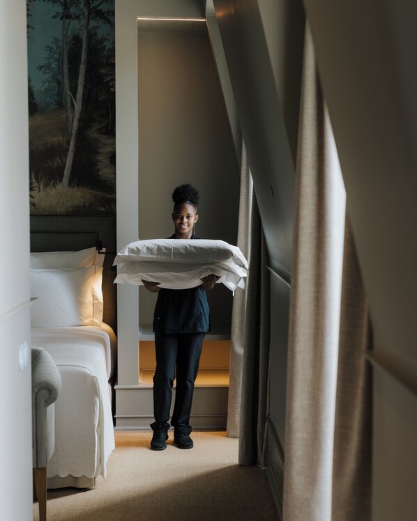 A person carrying a mattress in a hotel room with a bed, a painting, and a window with curtains. - AlmaLusa Alfama (Lisbon)