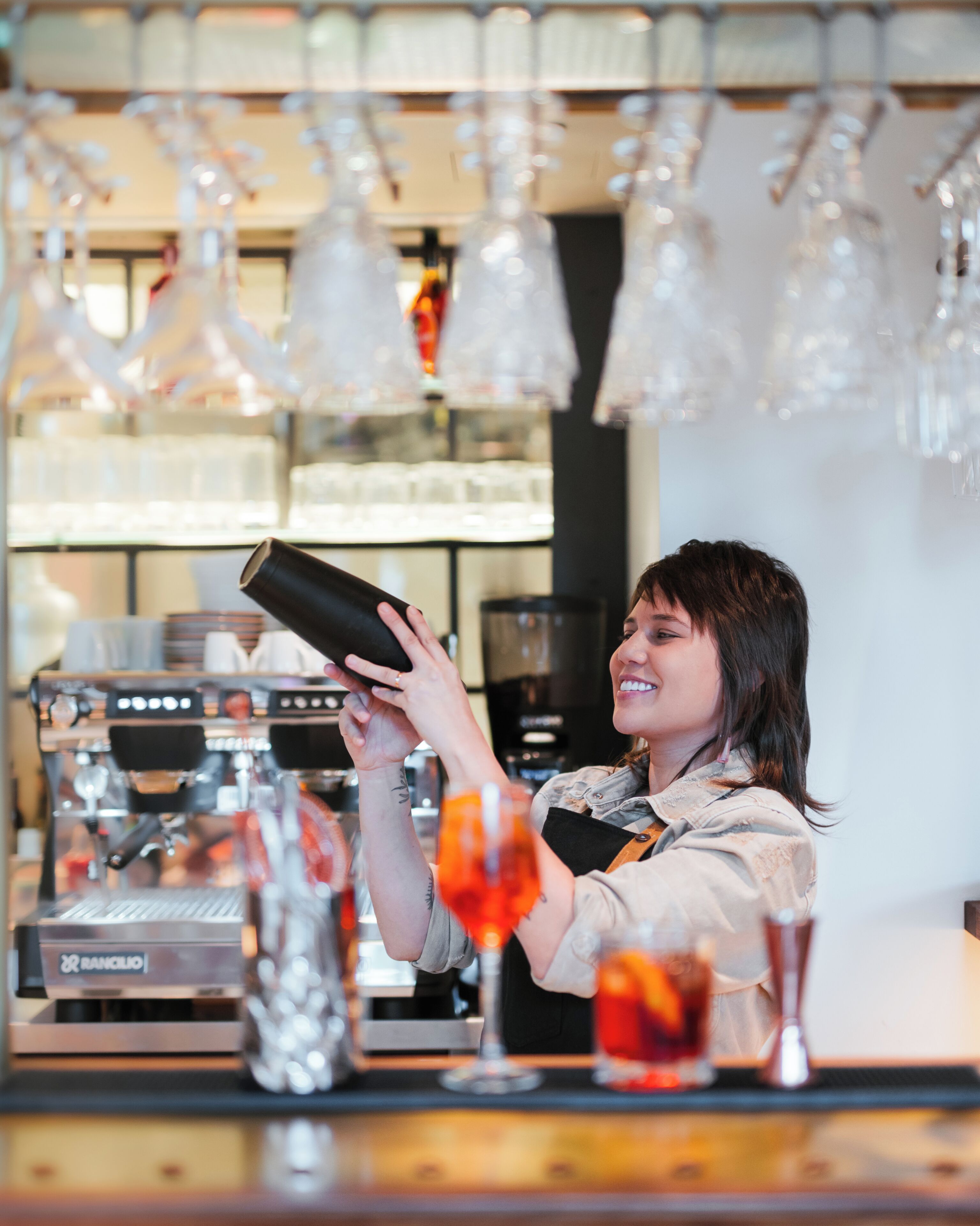 Un barista au travail, avec des machines à café et des verres en arrière-plan.