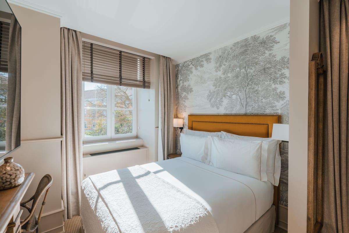 Hotelkamer met een bed, bureau, stoel, raam met gordijnen en een muurschildering van een boom.