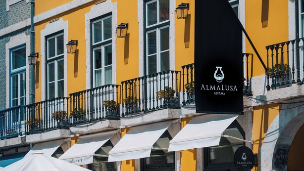 A yellow building with outdoor seating and a black flag with 'Almalusa' text.