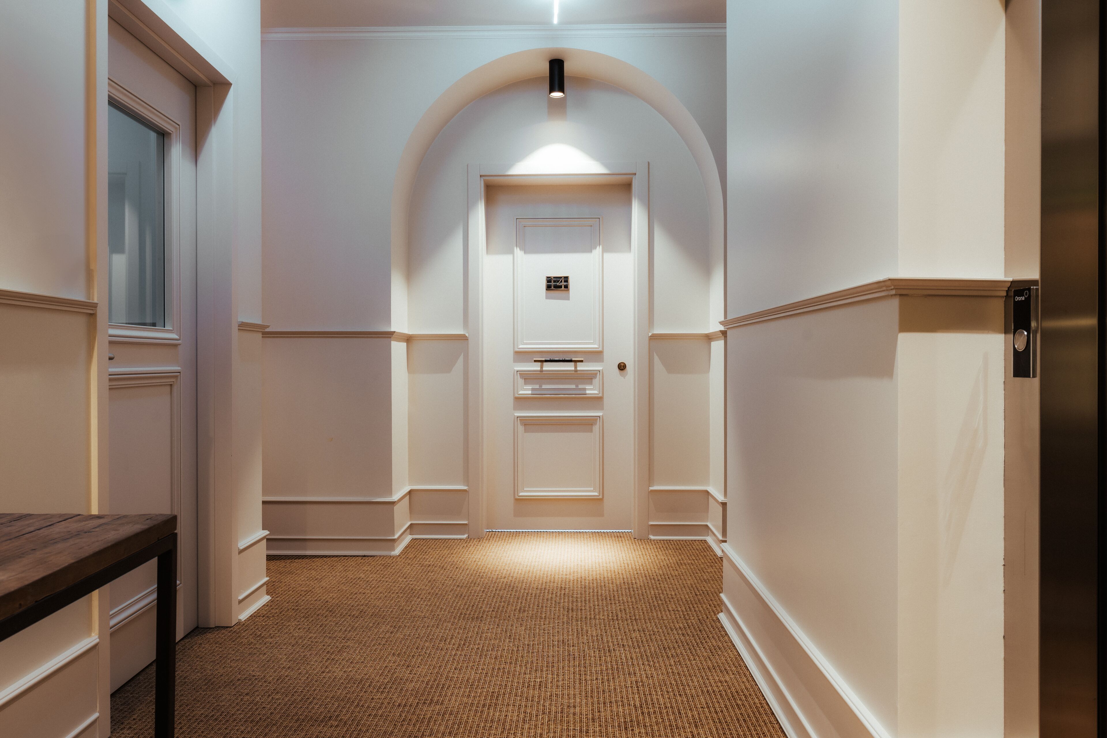 A hallway with a carpeted floor, white walls, and a wooden bench.