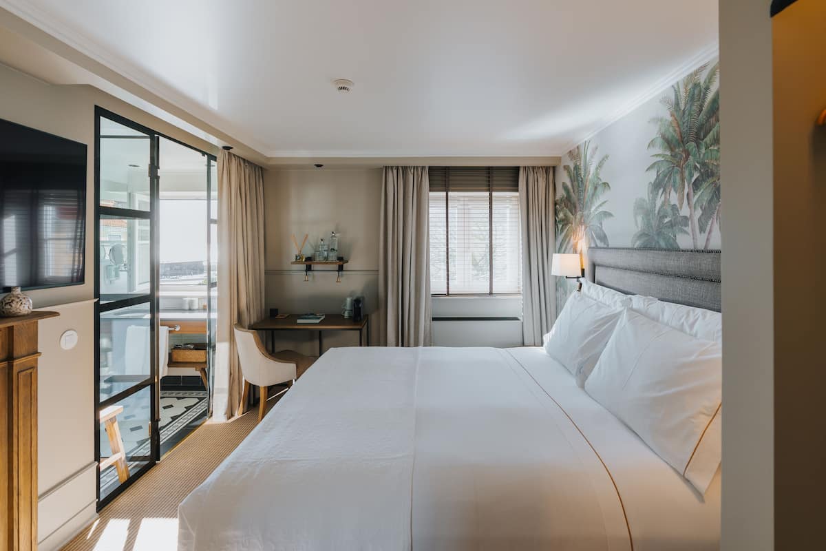 Een hotelkamer met een groot bed, een bureau met stoel, een televisie en een balkon met uitzicht.