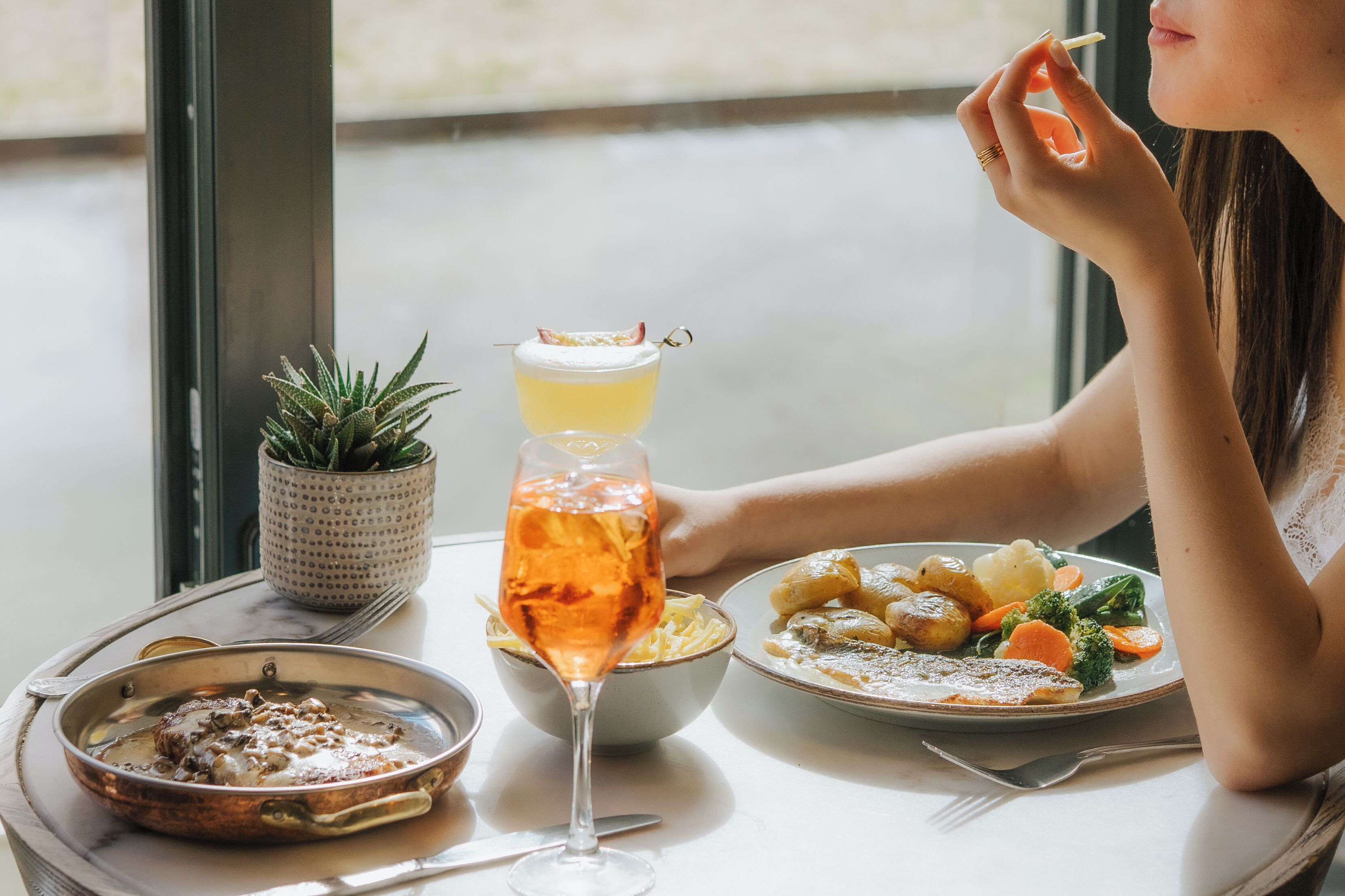 Una mesa de comedor con comida, un vaso de bebida y una planta en maceta.