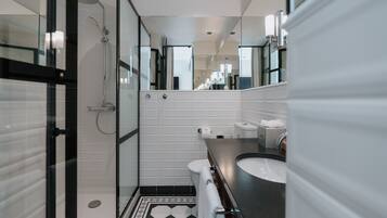 Een moderne badkamer met een glazen douchecabine, een witte betegelde wand, een zwart-wit vloertegelpatroon en een donker aanrecht met een wastafel.