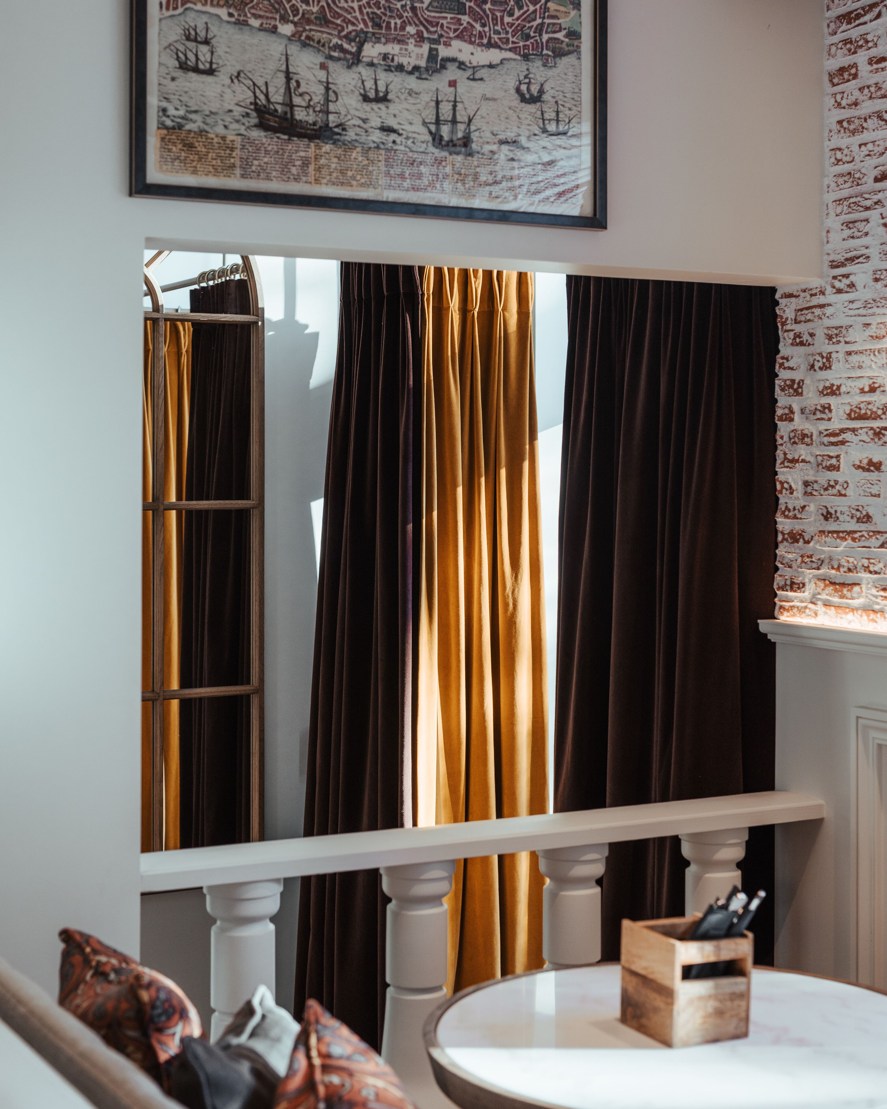 Una habitación con un ventanal grande, un mapa enmarcado en la pared, una mesa de madera con un juego de cuchillos, y un plaid estampado en el sofá.