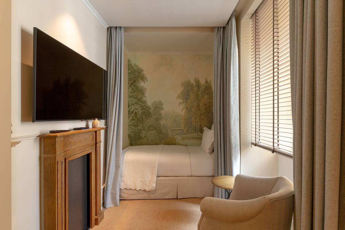 Een slaapkamer met een bed, een televisie, een stoel en een raam met gordijnen.