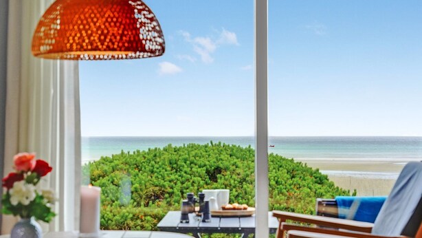 A balcony with a view of the beach, a table with a vase of flowers, and a hanging light fixture. - "Elpida" - 100m from the sea by Interhome (Glesborg)