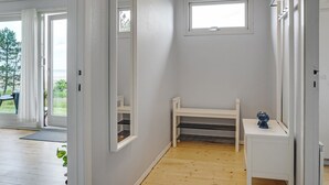 A room with a wooden floor, a white bench, a small table with a decorative item, a window, and a door leading to an outdoor area. - "Elpida" - 100m from the sea by Interhome (Glesborg)