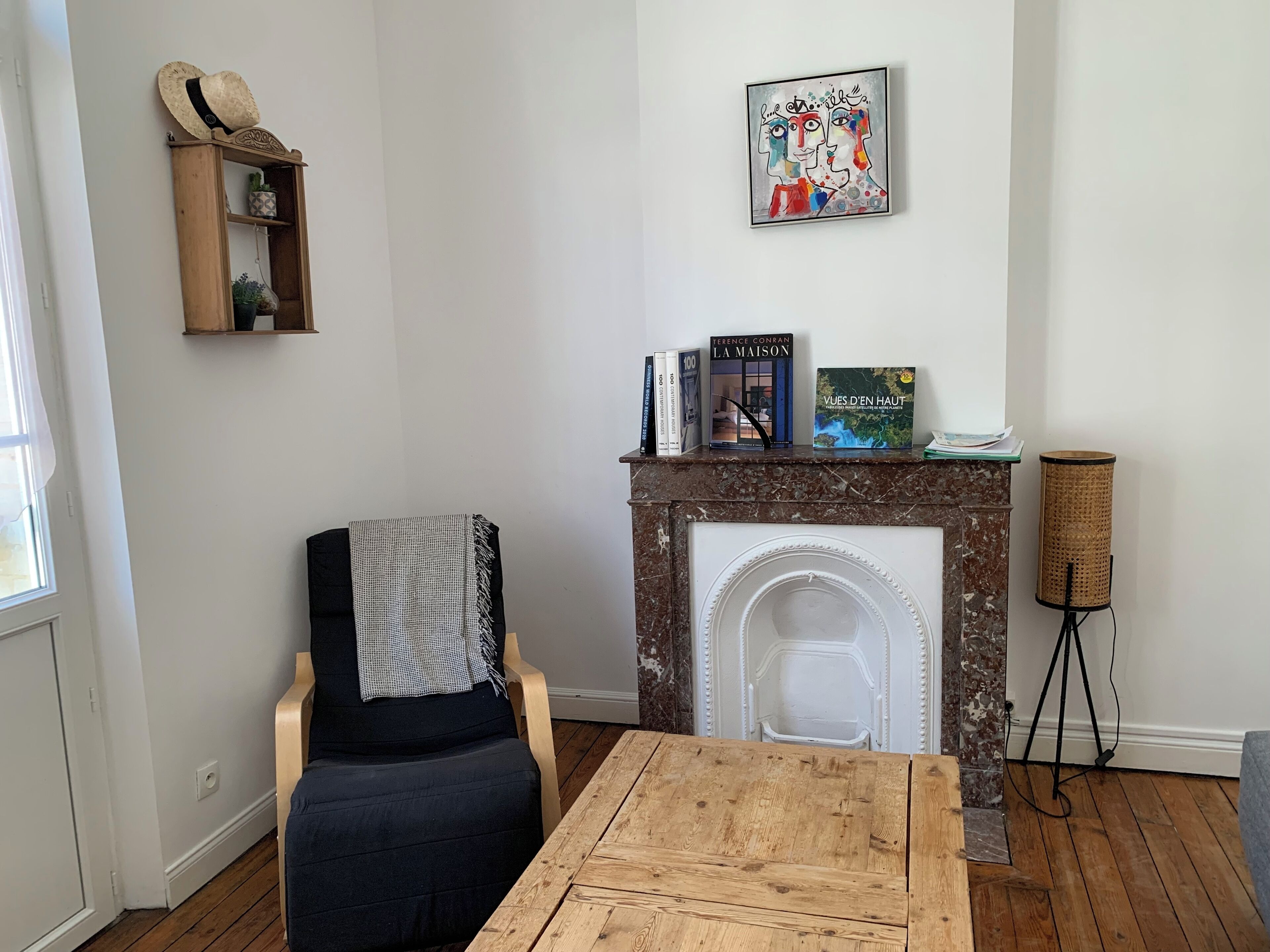 Una sala de estar con chimenea, una silla, una mesa, una estantería y un cuadro en la pared.