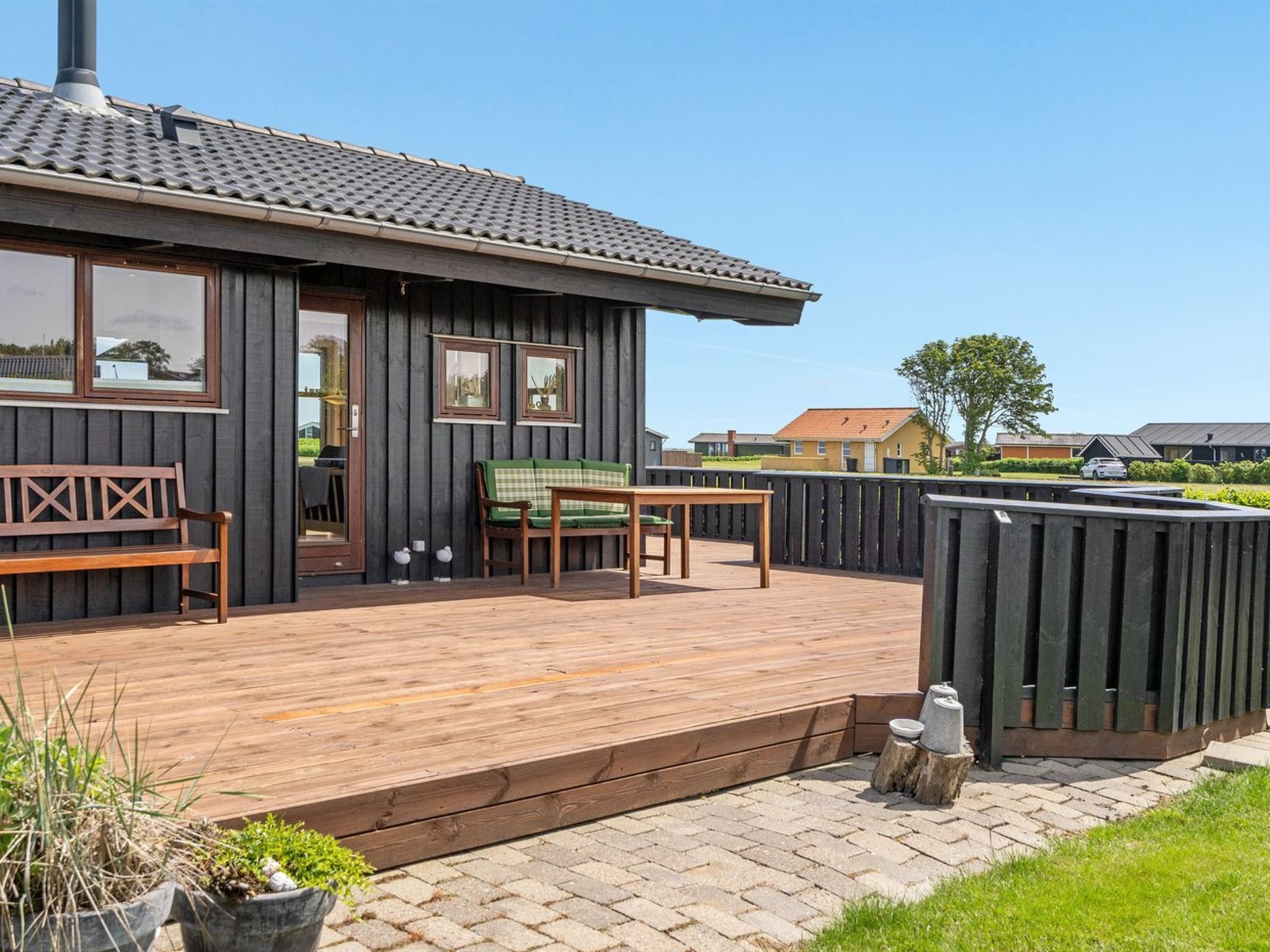 Un bâtiment moderne en bois doté d’une terrasse, d’un banc, d’une table et de deux fenêtres.
