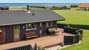 Een huis aan de kust met een terras, een bank en een tafel.