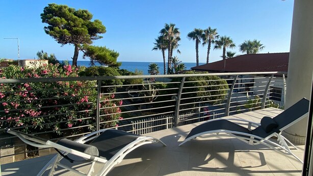 A balcony with two lounge chairs, a small table, and a view of the sea and palm trees. - Ripe Rosse ® -Residence- (Ogliastro Marina - Castellabate)