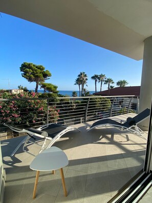 Un balcon avec deux fauteuils, une petite table et une vue sur la mer et les palmiers.