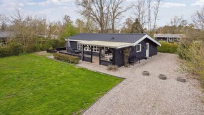 Een houten vakantiehuis met twee verdiepingen, een overdekte veranda en een oprit van grind.