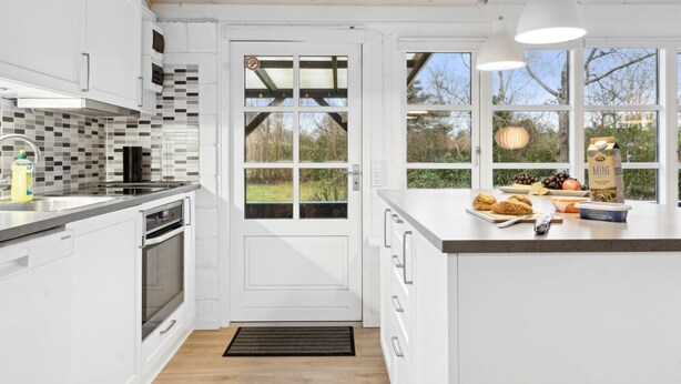 Een moderne keuken met witte kasten, een zwart betegelde spatwand en een groot raam met uitzicht op de omgeving.