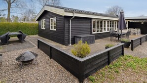 Een zwart houten huis met een terras, een barbecue en buiten zitplaatsen.