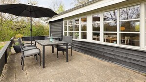 An outdoor patio with a table and chairs, a black umbrella, and a view of the interior through large windows. - "Mahalia" - 300m from the sea by Interhome (Sydals)