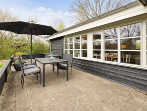 An outdoor patio with a table and chairs, a black umbrella, and a view of the interior through large windows. - "Mahalia" - 300m from the sea by Interhome (Sydals)