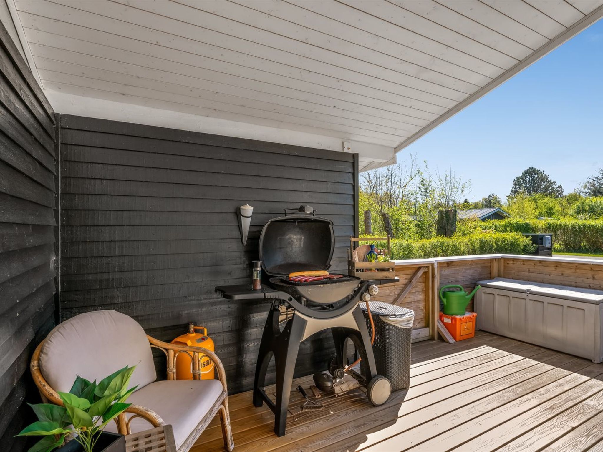 A covered outdoor area with a grill, a chair, a small table, and a trash bin.