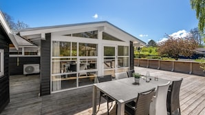 Un espace extérieur abrité, doté d’une table et de chaises, d’une grande fenêtre et offrant une vue sur le paysage environnant.