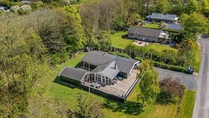 Une maison moderne dotée d’une grande terrasse, entourée d’une végétation luxuriante et située dans un cadre rural.