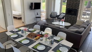 Ein modernes Wohnzimmer mit Essbereich, einer Sofagarnitur, einem Kamin und einem an der Wand montierten Fernseher.