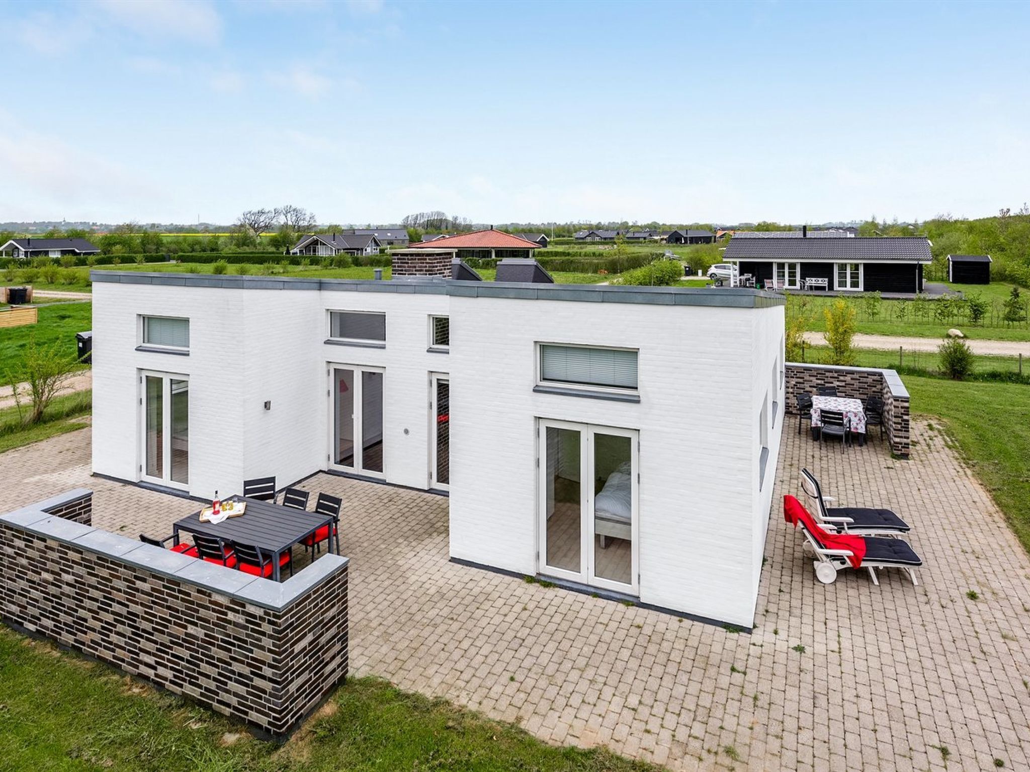 Une maison moderne à deux étages dotée d’un patio aménagé avec du mobilier d’extérieur et un barbecue.