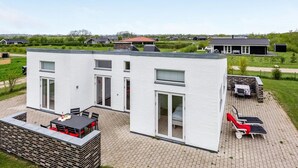 Ein modernes, zweistöckiges Haus mit einer Terrasse, die Gartenmöbel und eine Grillmöglichkeit bietet.