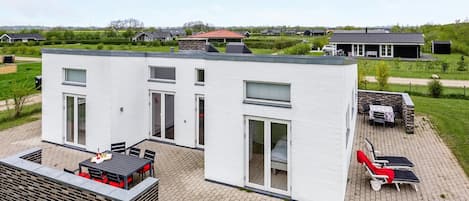 A modern two-story house with a patio area featuring outdoor furniture and a barbecue setup.