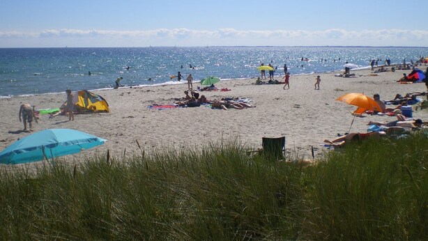 Ein Strand mit Menschen, die sich sonnen und schwimmen, Zelten und Sonnenschirmen.
