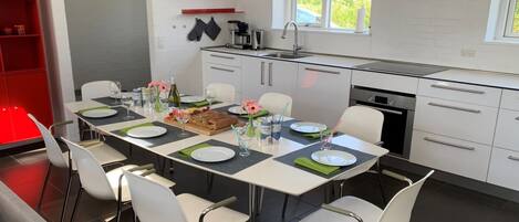 A modern kitchen with a dining area, white cabinets, a built-in oven, and a window overlooking greenery.