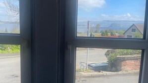 A window with a view of a road, a building, and a body of water. - Studio Apartments (Langbank)