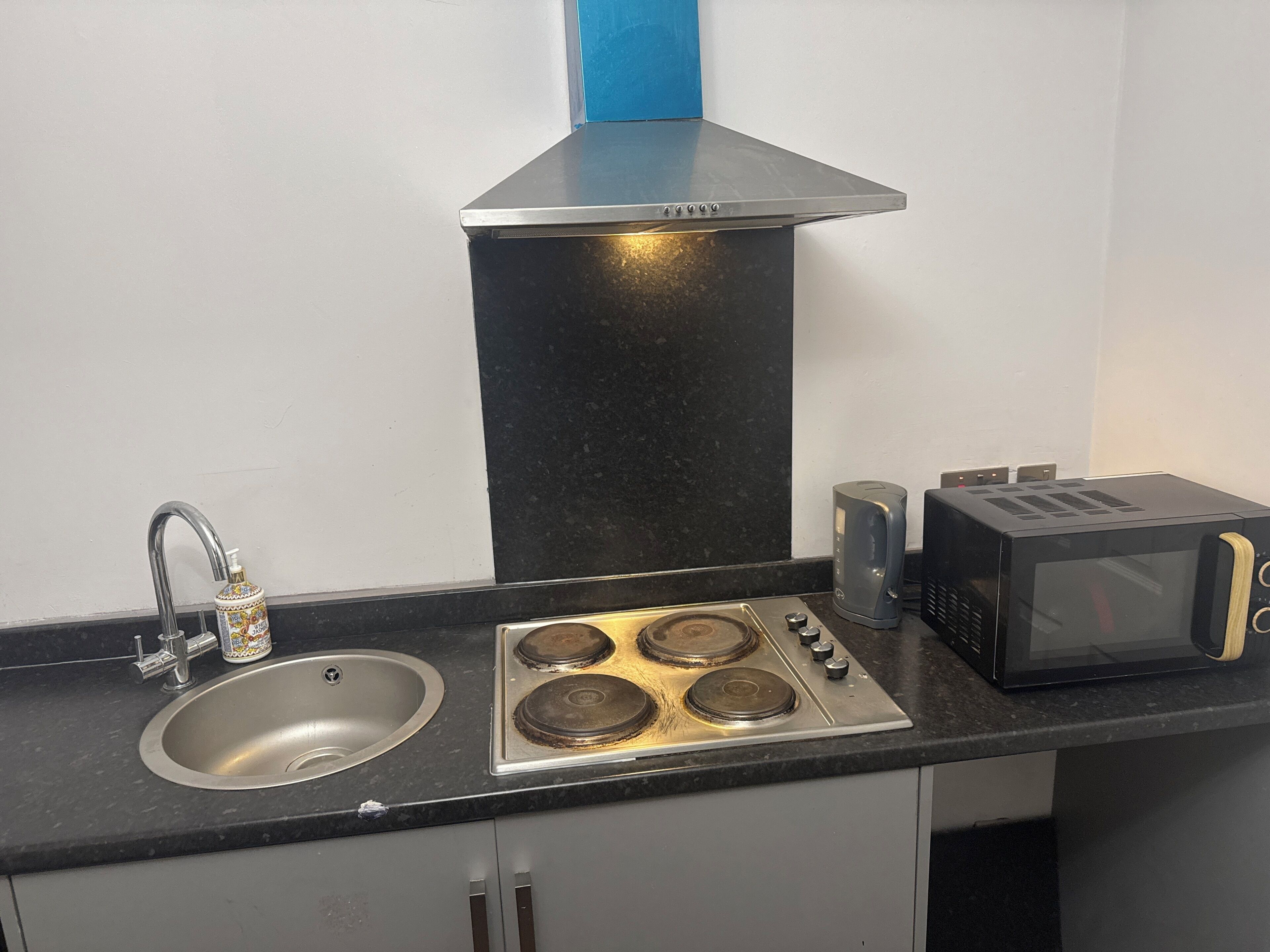 Una cocina con un lavamanos de acero inoxidable, una estufa a gas, un microondas y una campana extractora azul.