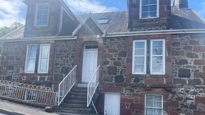A stone building with a staircase leading to a door, a small porch with a railing, and a clear sky. - Studio Apartments (Langbank)