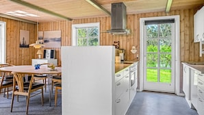 A modern kitchen with wooden walls, a dining area with a table and chairs, and a large window with a view of greenery. - "Nanja" - 759m from the sea by Interhome (Løkken)