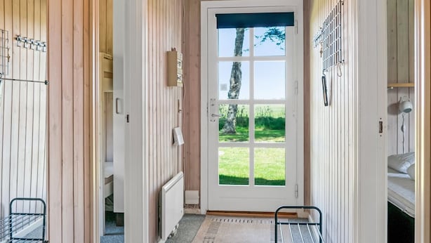 A hallway with wooden paneling, a white door with a window, and a radiator on the floor. - "Nanja" - 759m from the sea by Interhome (Løkken)